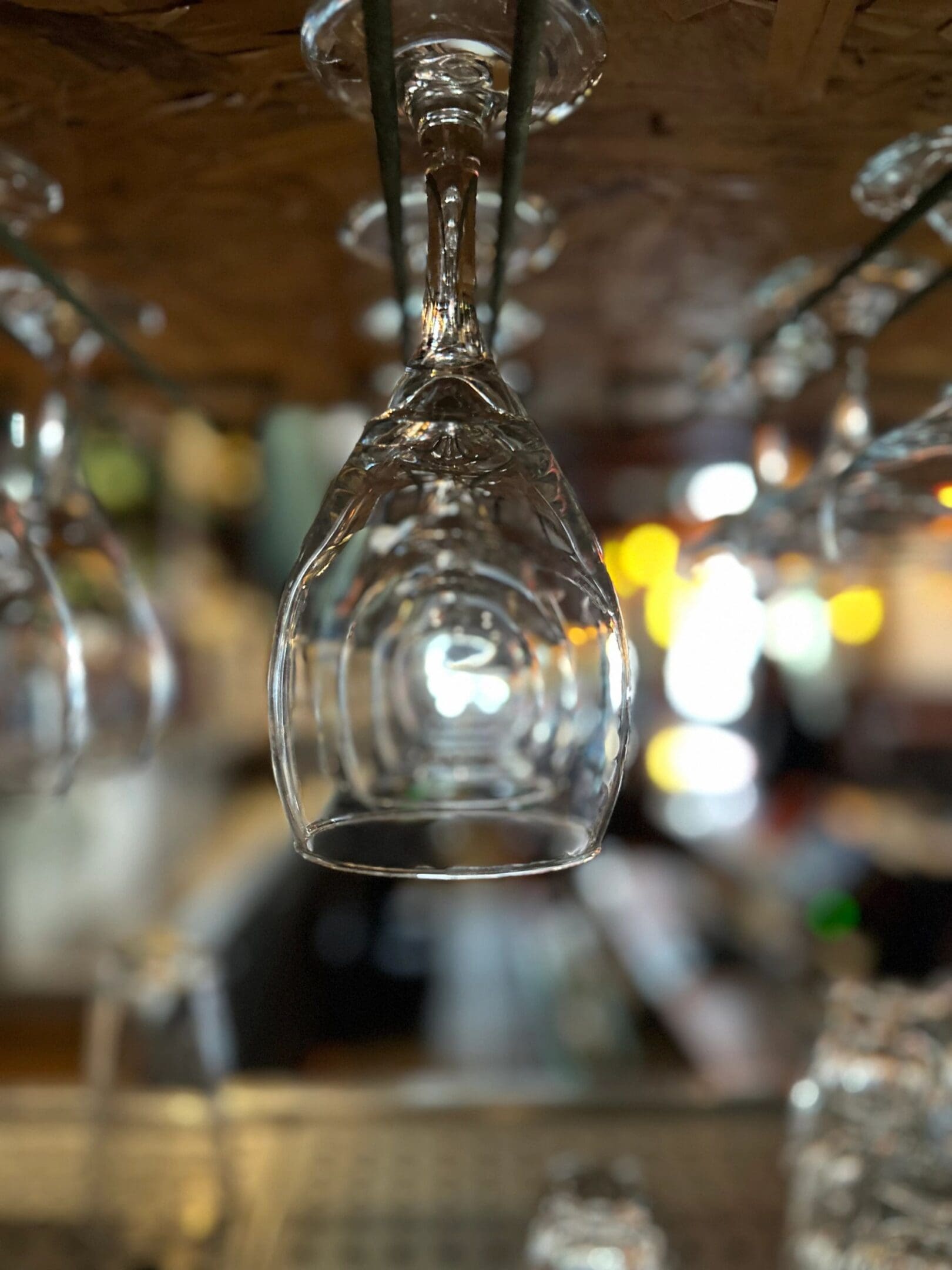 Rows of hanging wine glasses at a bar with a blurred background.