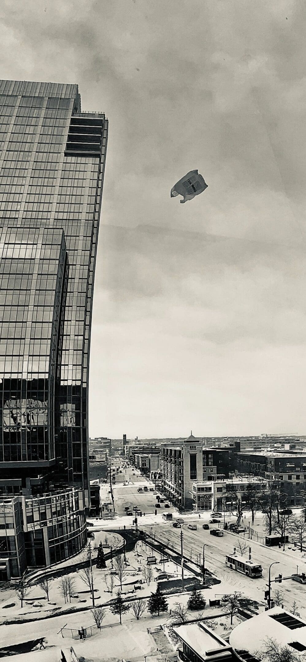 A plastic bag floats above a snowy cityscape with tall buildings and streets below.