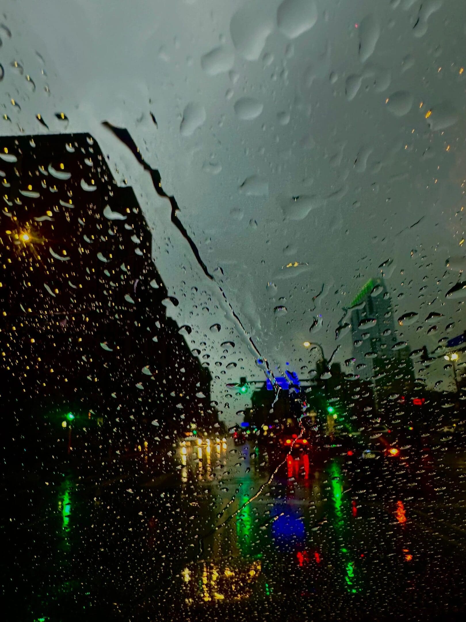 City street at night blurred by raindrops on a window with colorful lights reflecting.