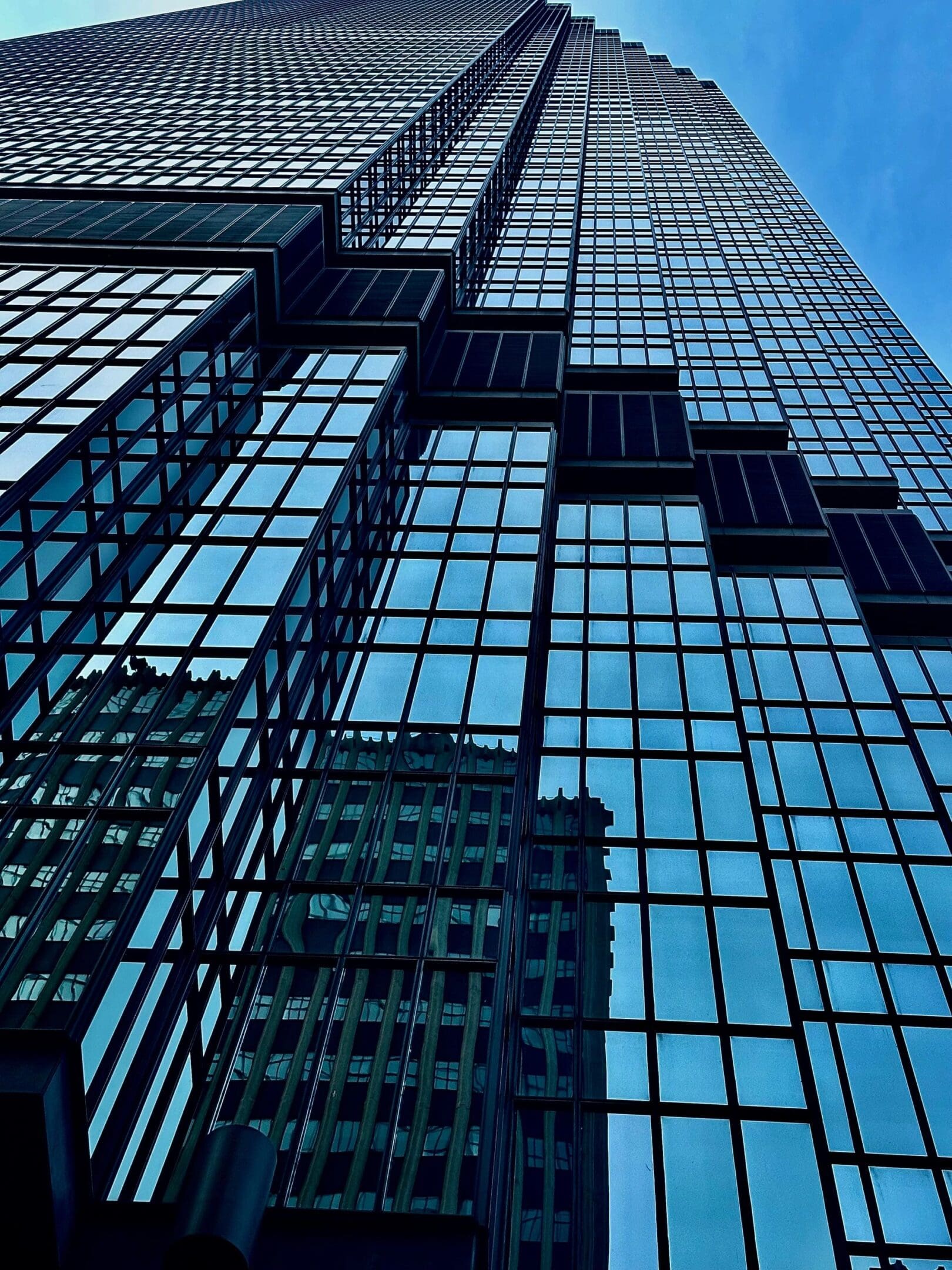Looking up at a towering glass skyscraper with reflections of another building.