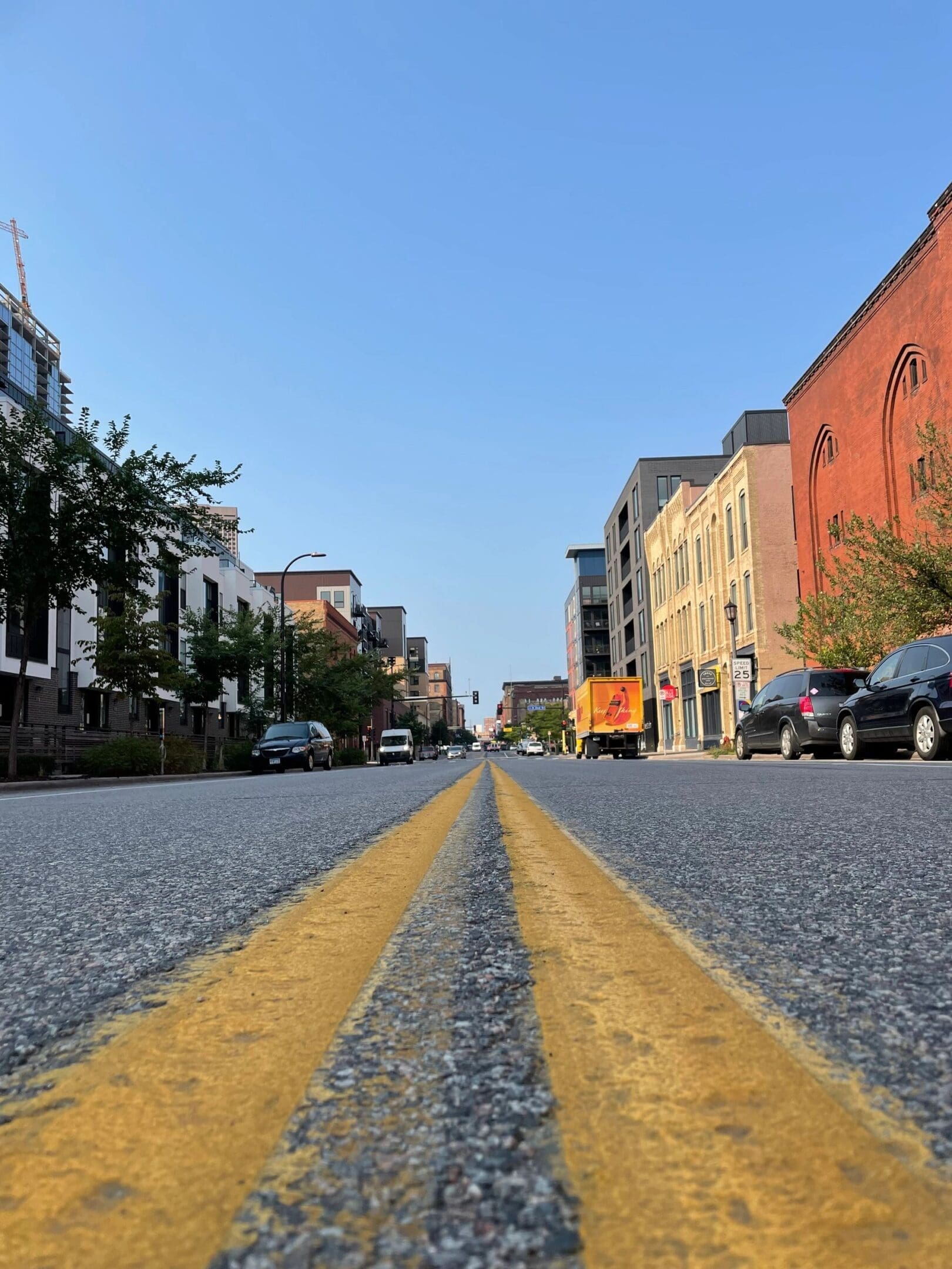 City street with yellow dividing lines and parked cars on both sides.