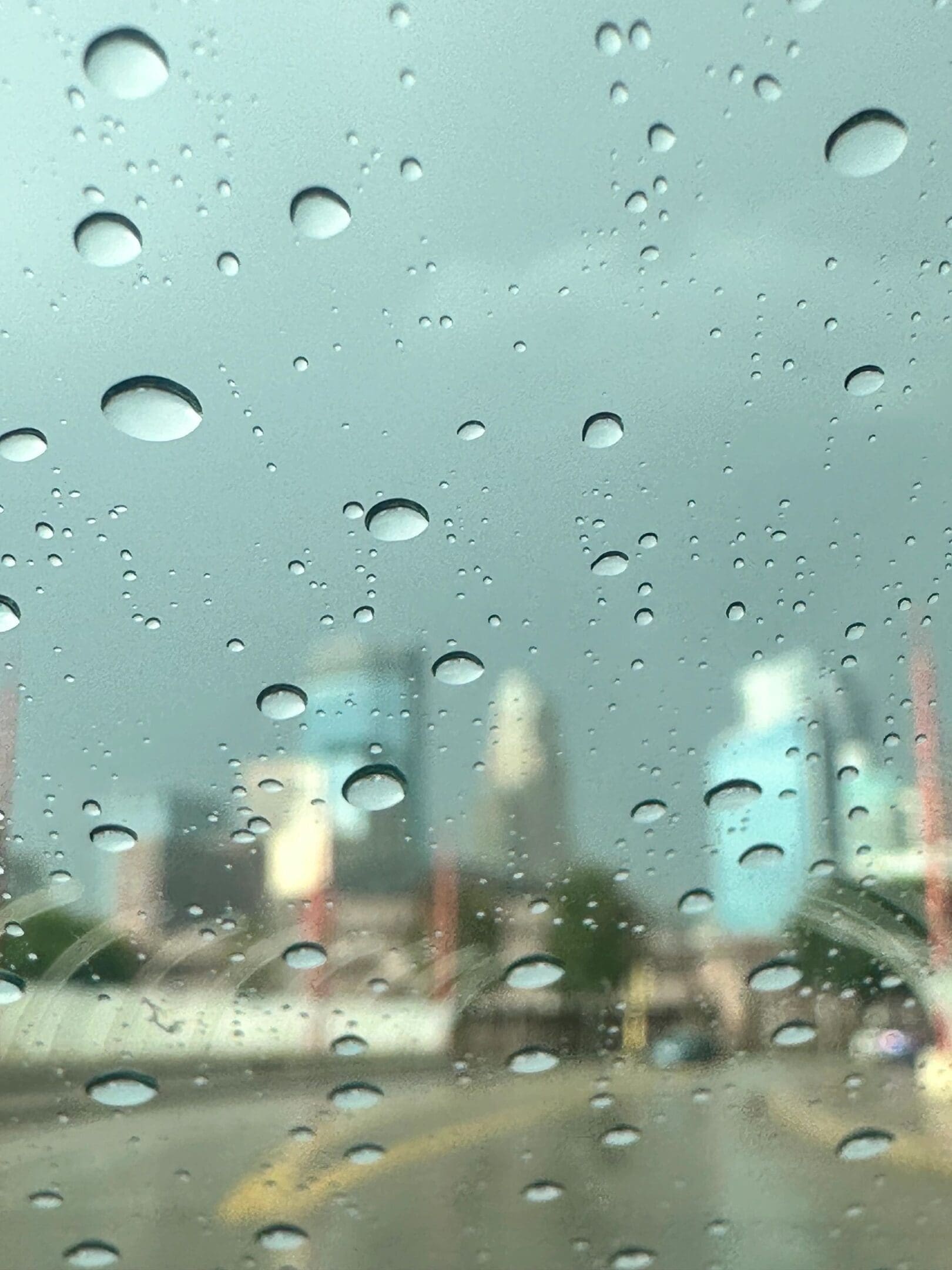 Raindrops on a window with a blurry city skyline in the background.