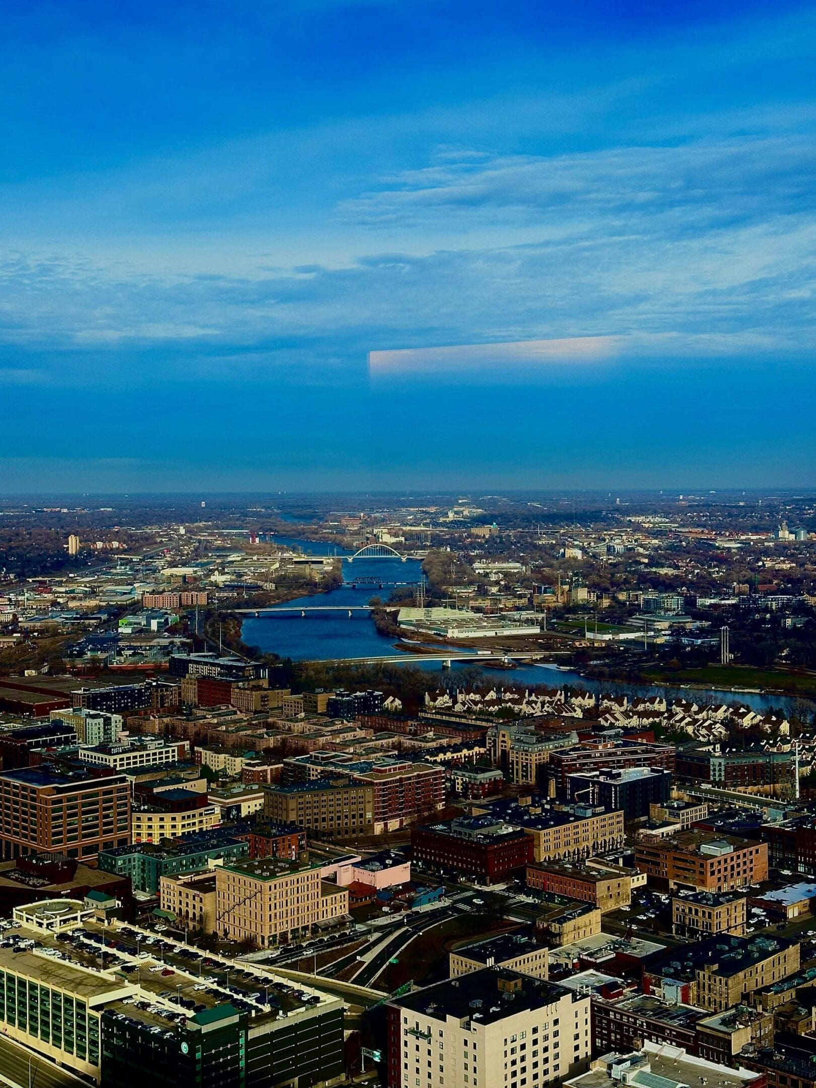 Aerial view of a city with multiple bridges over a winding river under a vast blue sky.