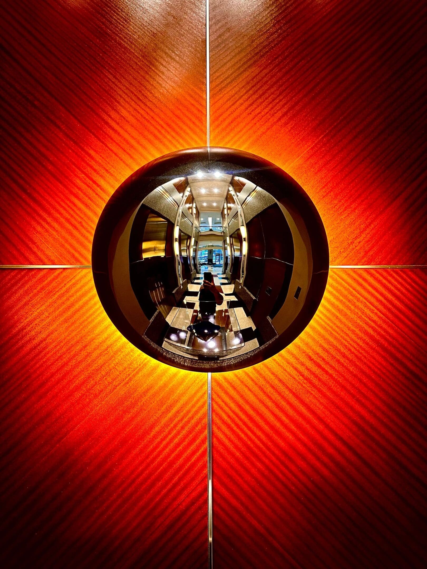 A reflective spherical surface on a vibrant orange wall showing a hallway reflection.