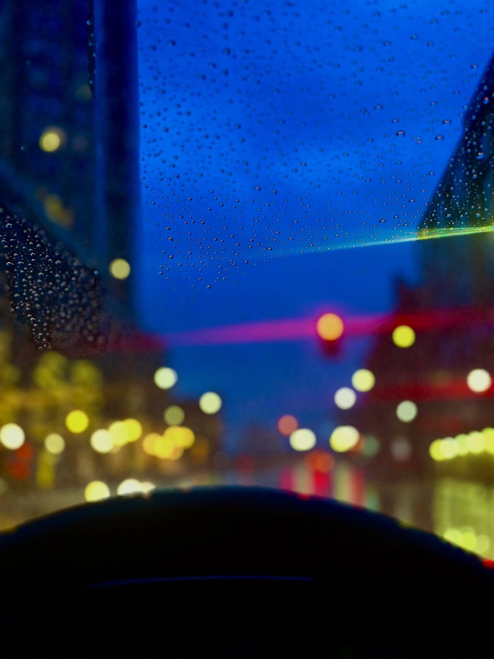 Raindrops on a car windshield with blurred city lights at night.