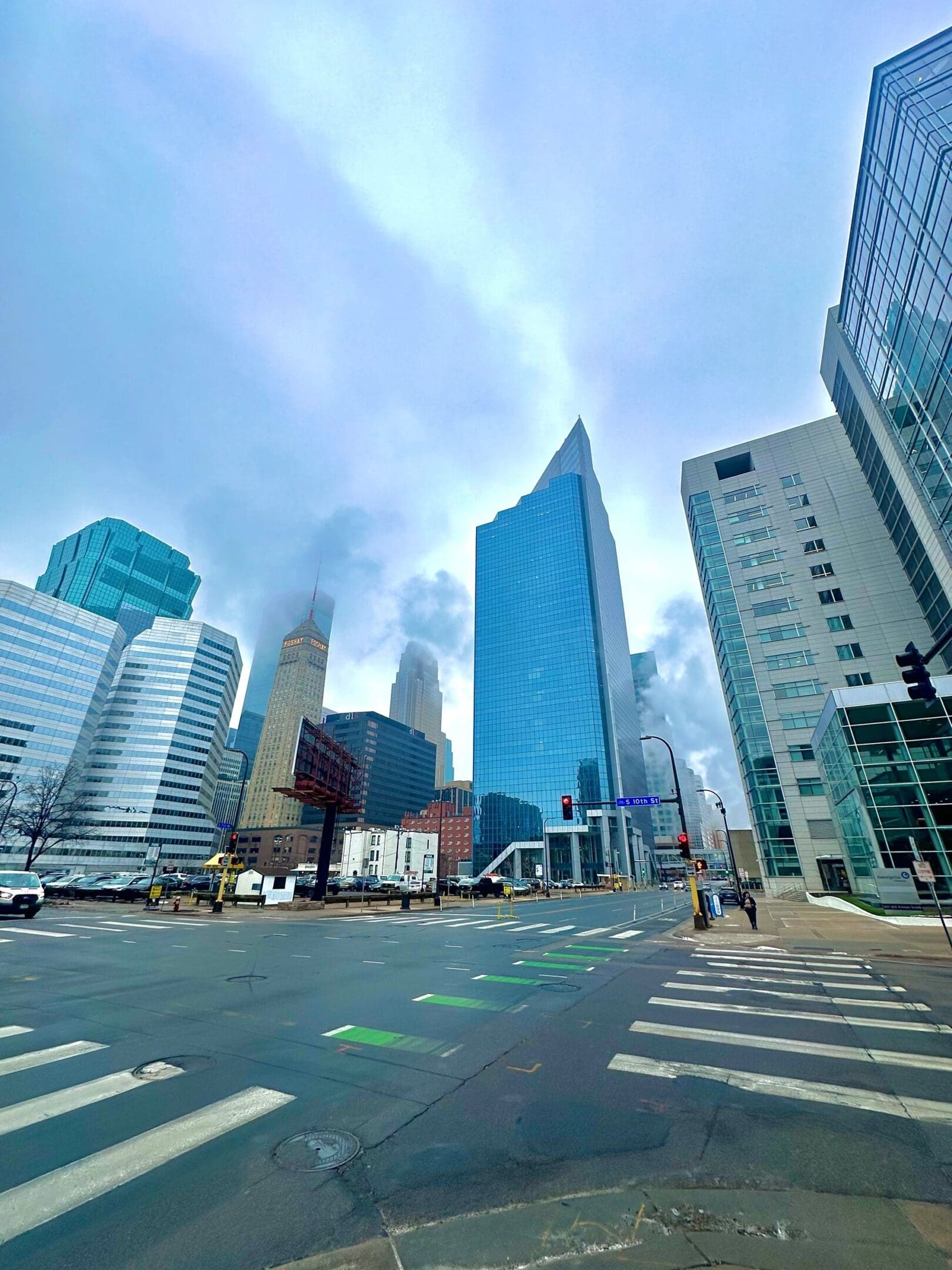 Foggy cityscape with modern skyscrapers and empty streets under a cloudy sky.