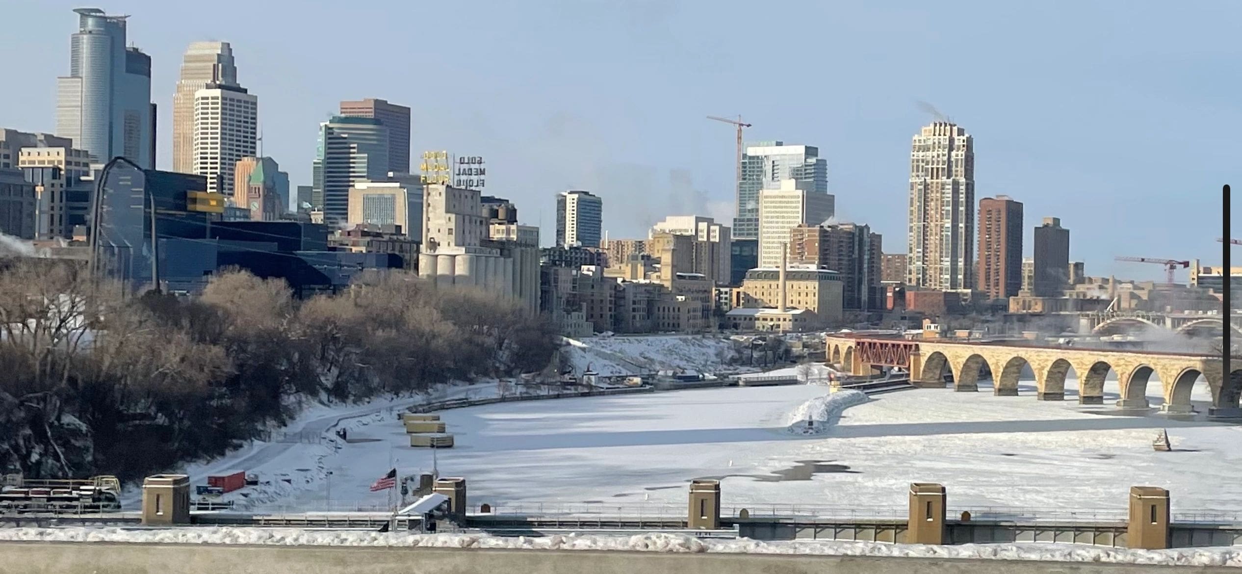 Winter view of a frozen river and city skyline with a stone arch bridge.