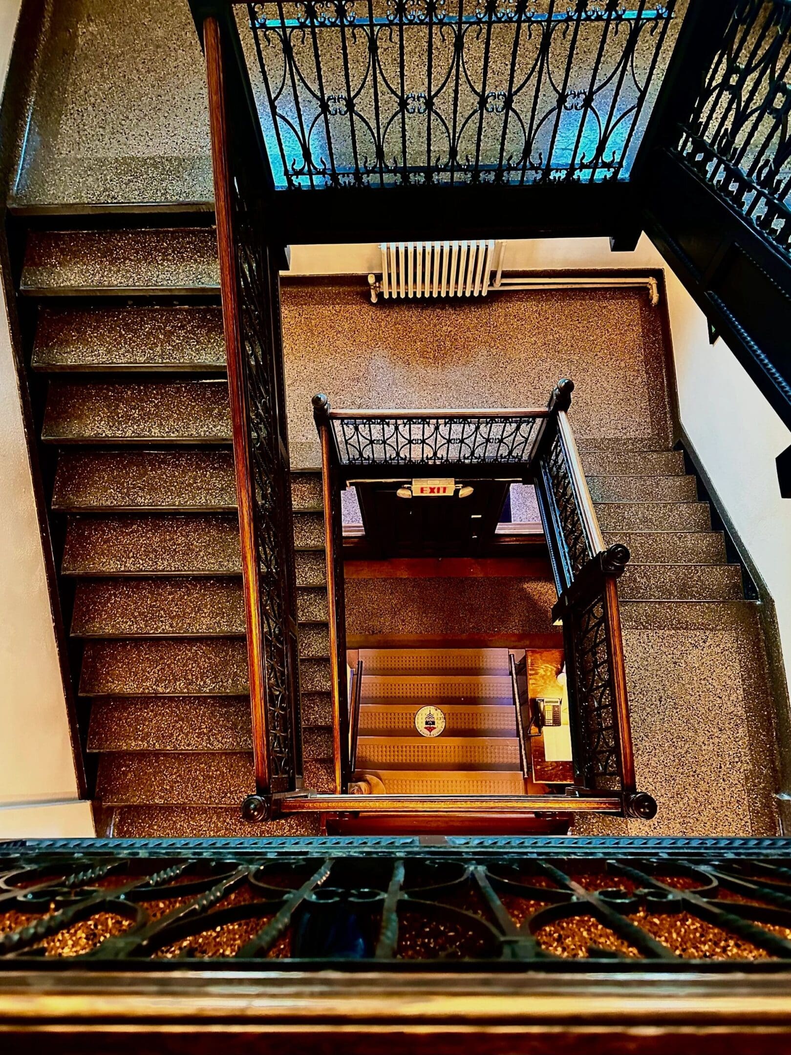 Top view of a vintage staircase with intricate railings and an exit sign.