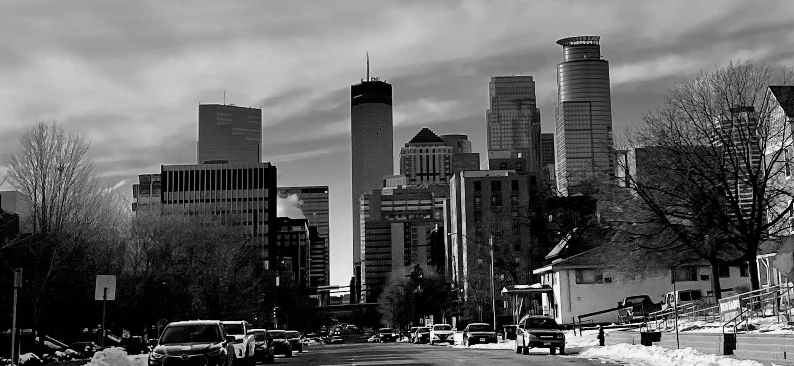 Black and white city skyline with cars on a snowy street.