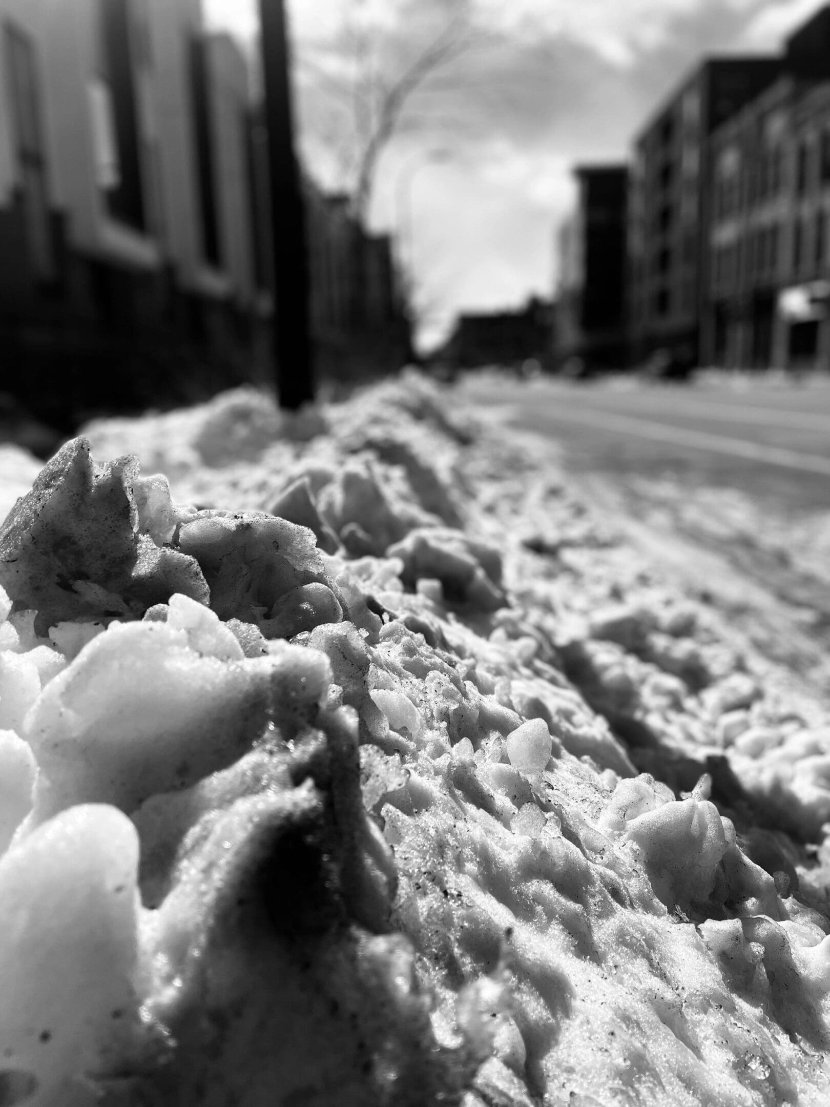 Close-up of dirty snow piled along an urban street in black and white.